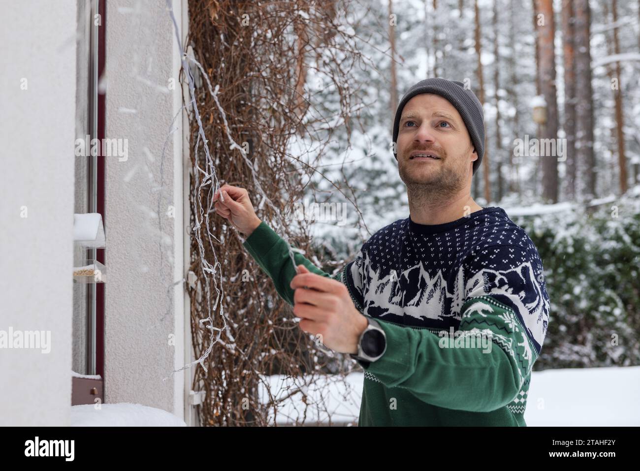 man decorating house exterior with christmas lights on snowy winter day Stock Photo