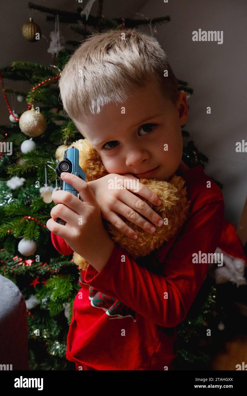 A child in red hugs a teddy bear and a car near a christmas tree Stock ...