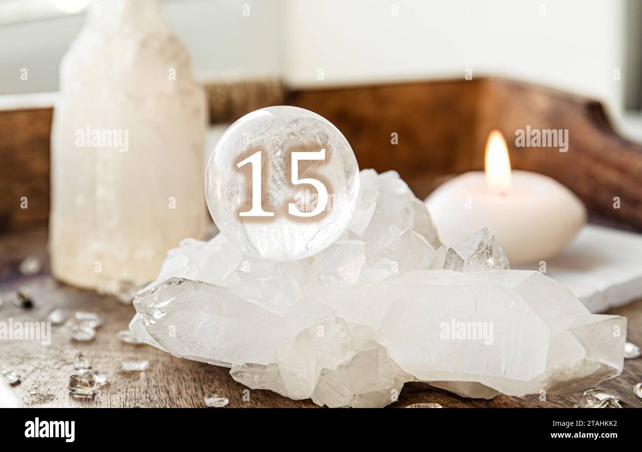 Number fifteen on Gemstone sphere or crystal balls known as crystallum orbis and orbuculum. Natural clear quartz ball on stand on wood tray in home. Stock Photo