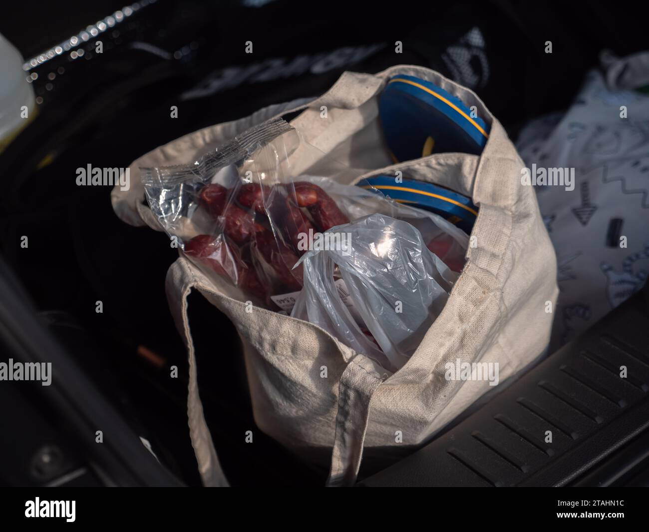 A bag with smoked sausages, snacks, and thong shoes to change in an open car trunk at a stopover. Travel road trip concept. Stock Photo