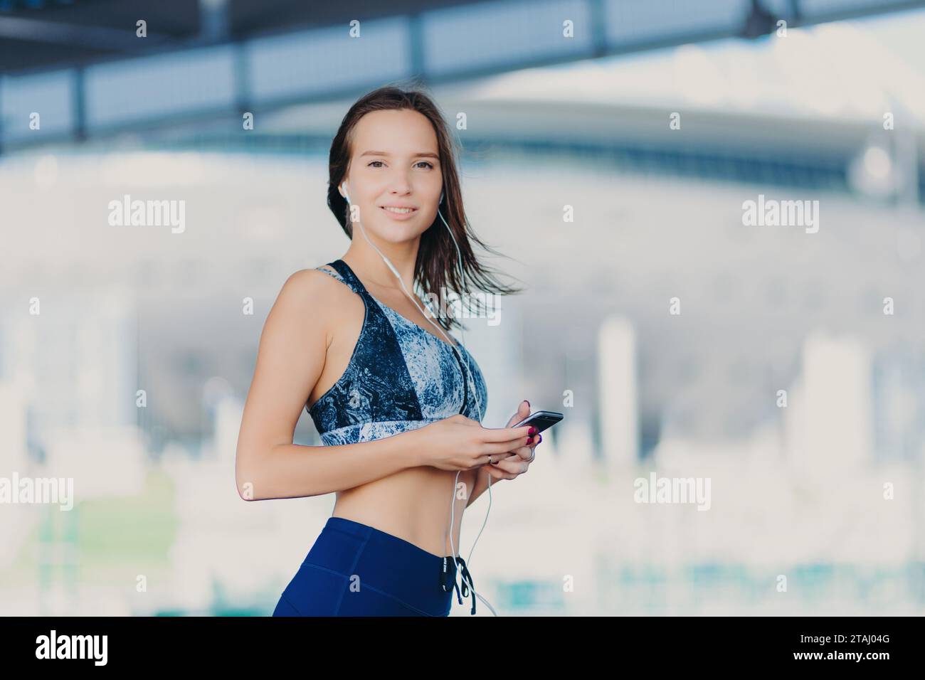 Confident woman in sportswear with headphones and smartphone, urban setting Stock Photo