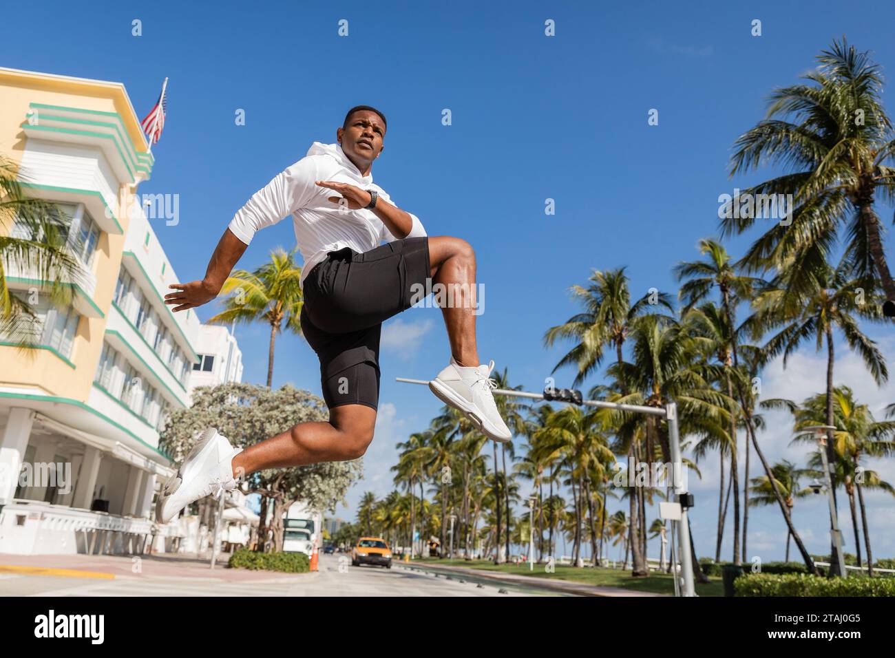 sportive african american man jumping next to palm trees and modern condominium in Miami Stock Photo