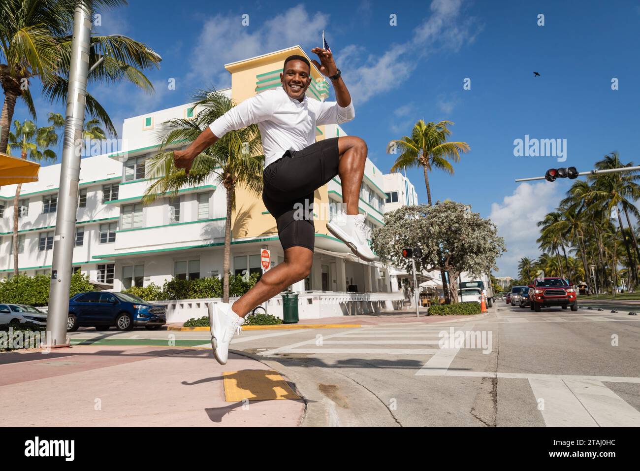 cheerful african american man jumping next to palm trees and modern condominium in Miami Stock Photo