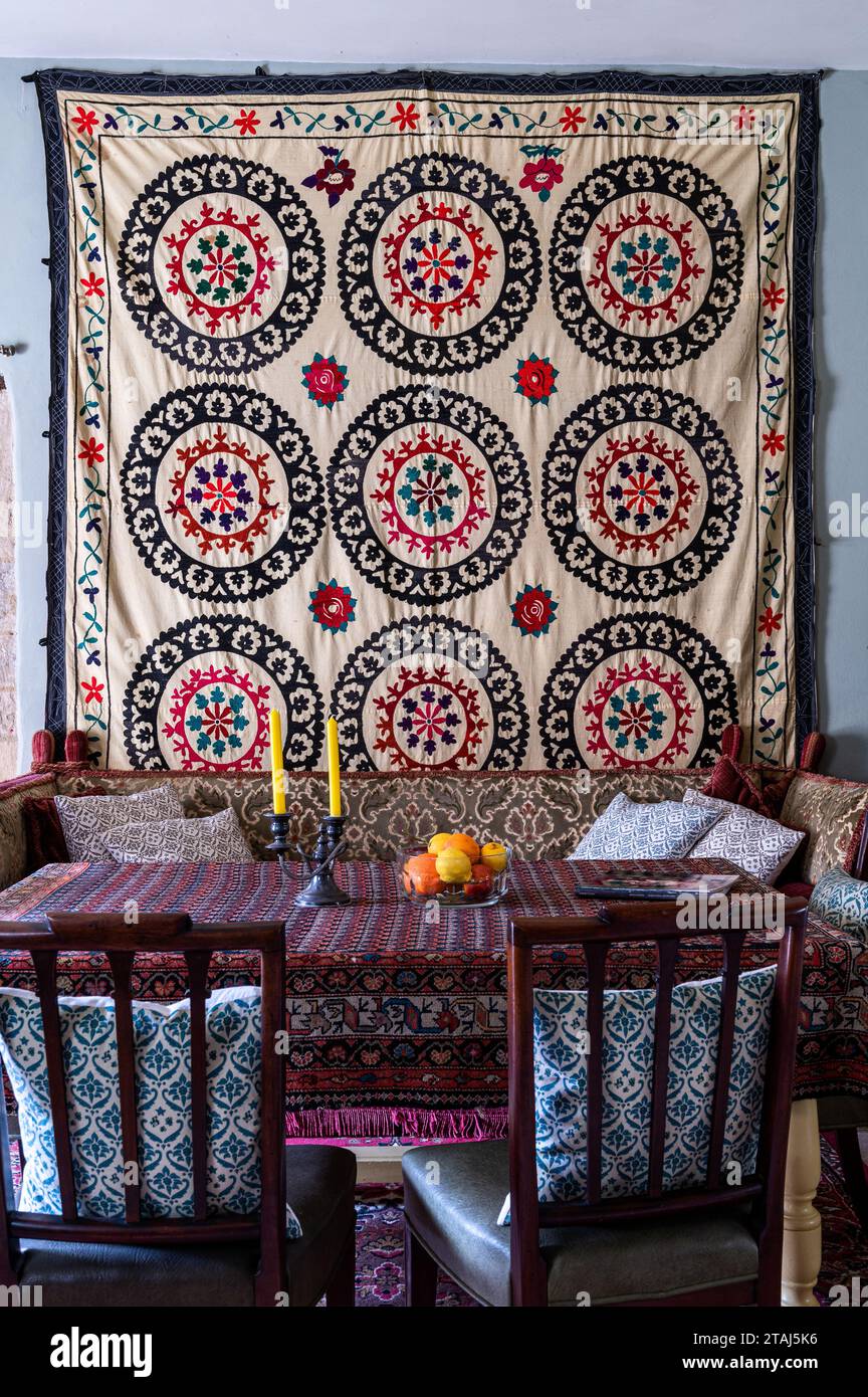 Suzani wall hanging with rug used as tablecloth on dining table in Georgian barn conversion, Tetbury, Gloucestershire, UK. Stock Photo