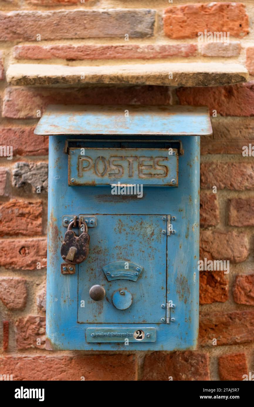 An antique, weathered, blue, metal letter box on a red brick wall with the words Postes, meaning letters and in French, below, 'Number of pick ups per Stock Photo
