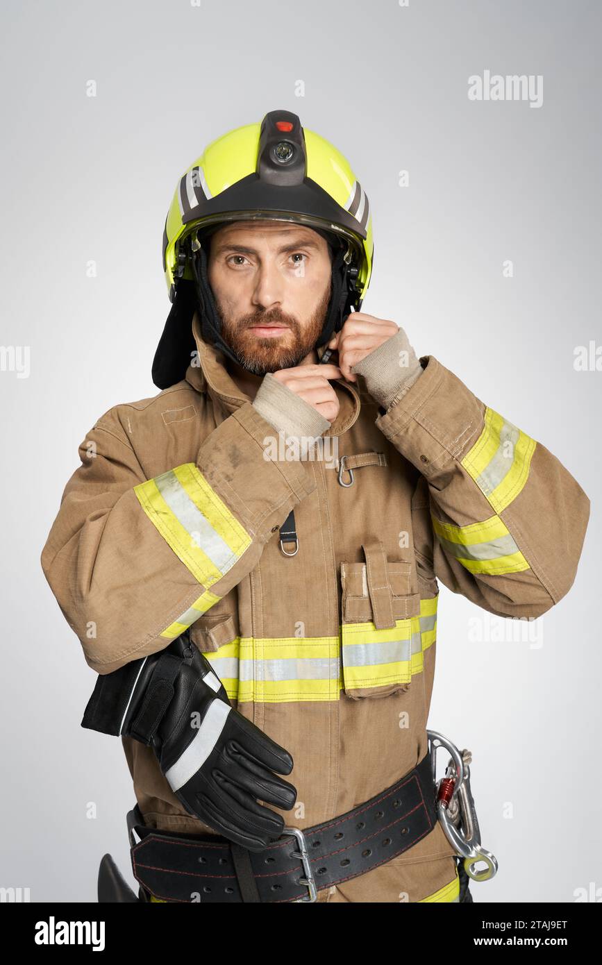 Serious male firefighter in uniform wearing protective helmet indoor