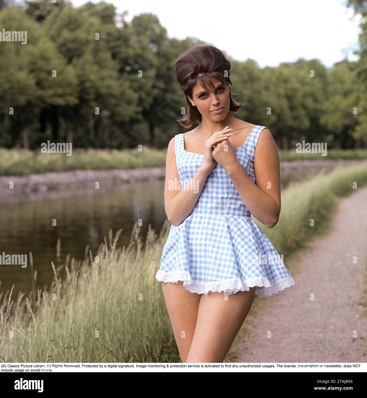 In the 1960s. A dark-haired girl pictured wearing a short chequered patterned dress. 1969 Stock Photo