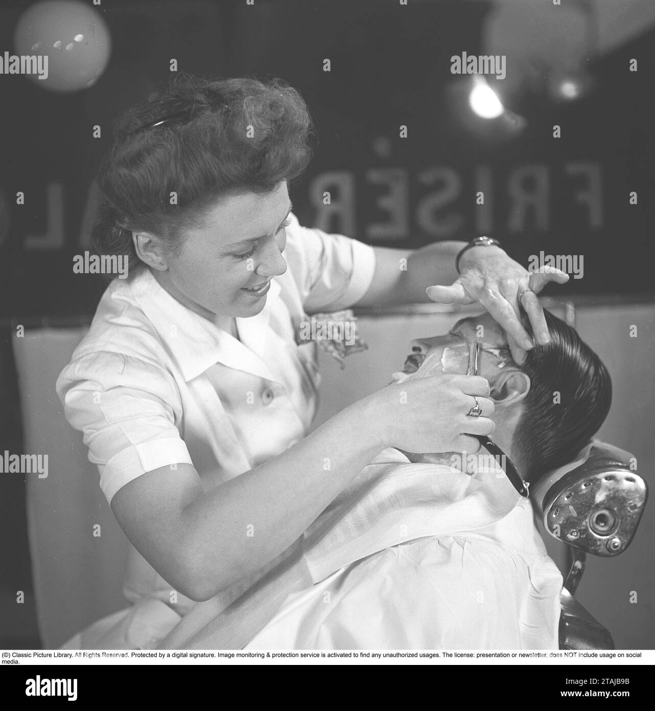 Getting a shave in the 1940s. A young woman is shaving a man at the