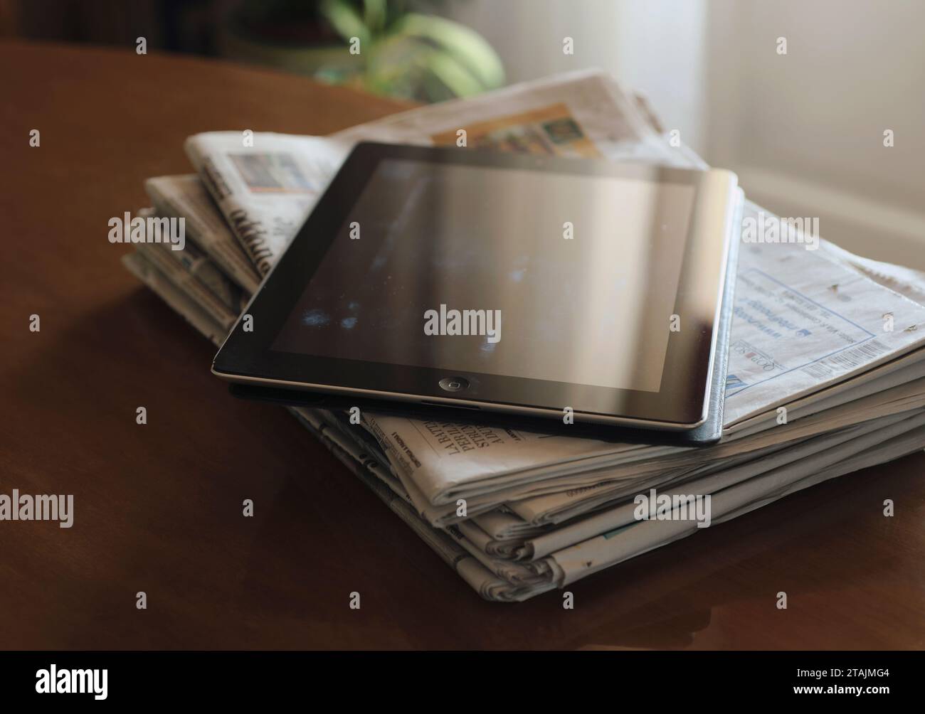 sunlight reflections on digital tablet screen and stack of newspapers on table Stock Photo