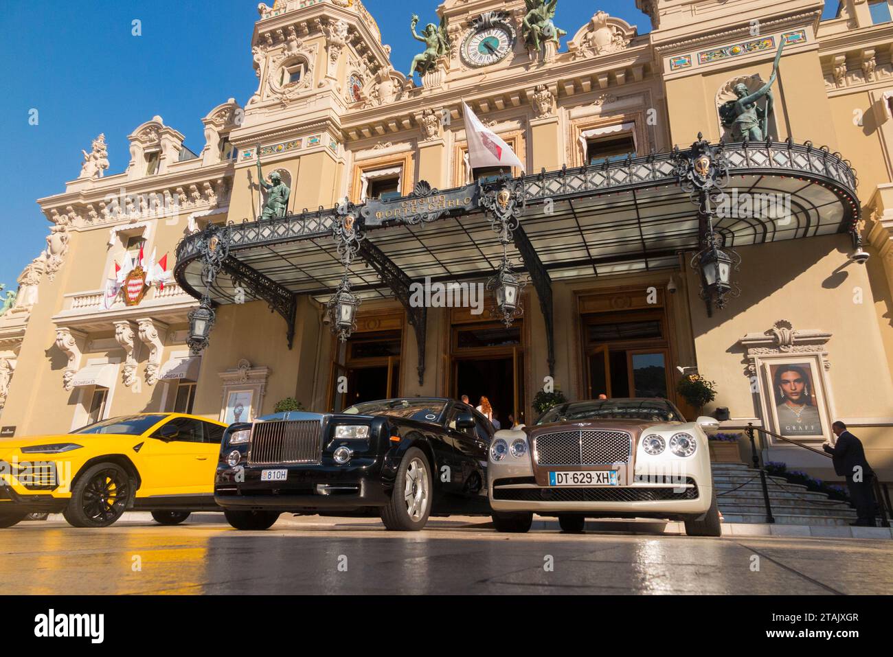 Expensive cars, people viewing them and the exterior of Monte Carlo / Monte-Carlo Casino, Monaco. Sunny summer day with sun and blue sky / skies. (135) Stock Photo