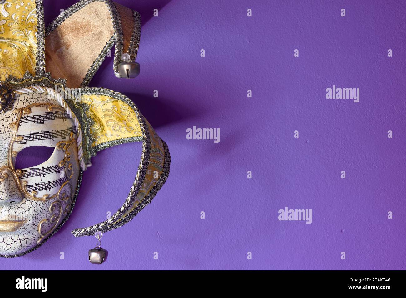 Front view of fancy golden Venetian carnival mask hanging on purple wall. Copy space for text. Stock Photo