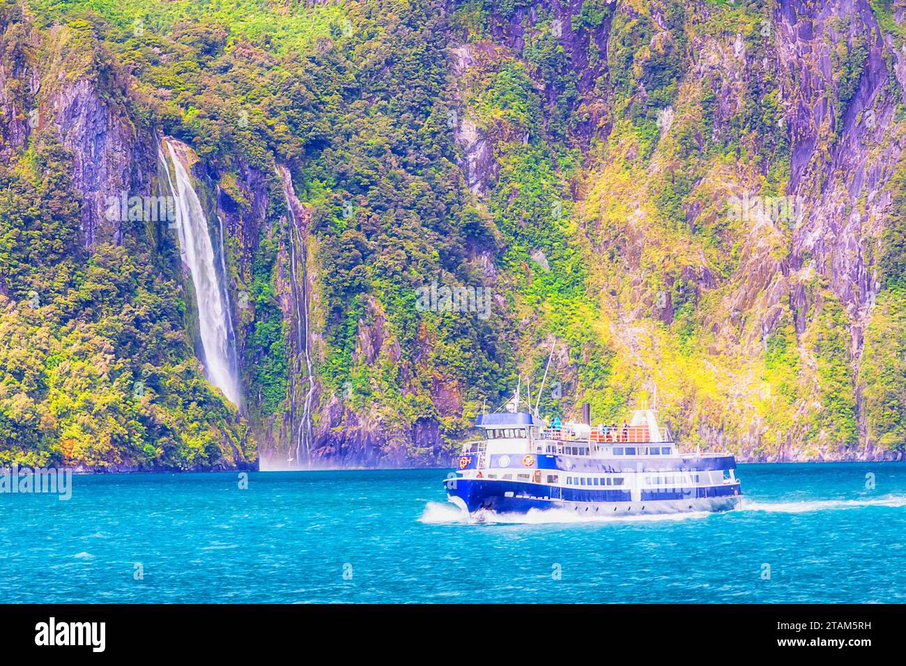 Exploratory cruise ship with tourists on board at Stirling waterfall in Milford Sound fiordland of New Zealand. Stock Photo