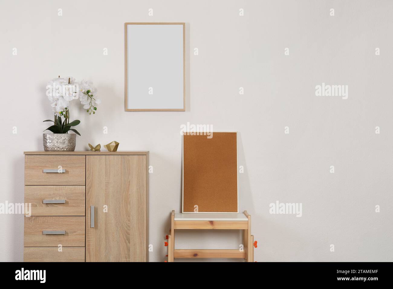 Chest of drawers, table, orchid and picture frames indoors, space for text. Interior design Stock Photo
