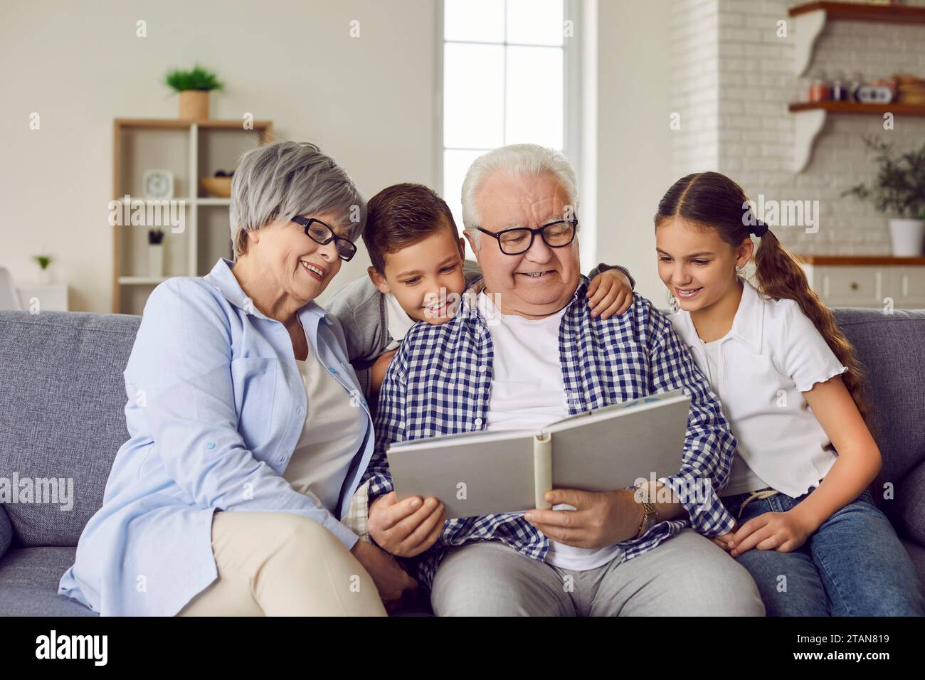 Happy grandparents and children sitting on the couch and reading a book together Stock Photo