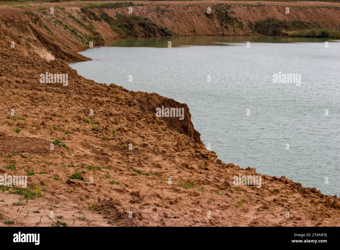 Clay soil on the edge of a flooded sand pit, dangerous cliff Stock