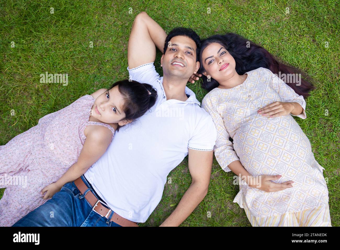 Happy Young indian couple with their cute daughter lying in park or ...