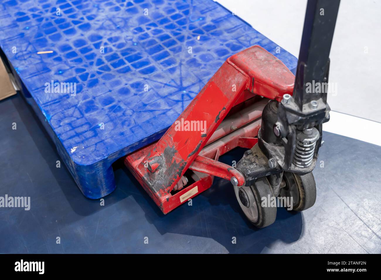 A manual hydraulic pallet lift stands on the warehouse floor, ready to transport heavy pallets of goods in a bustling store. The industrial setting co Stock Photo