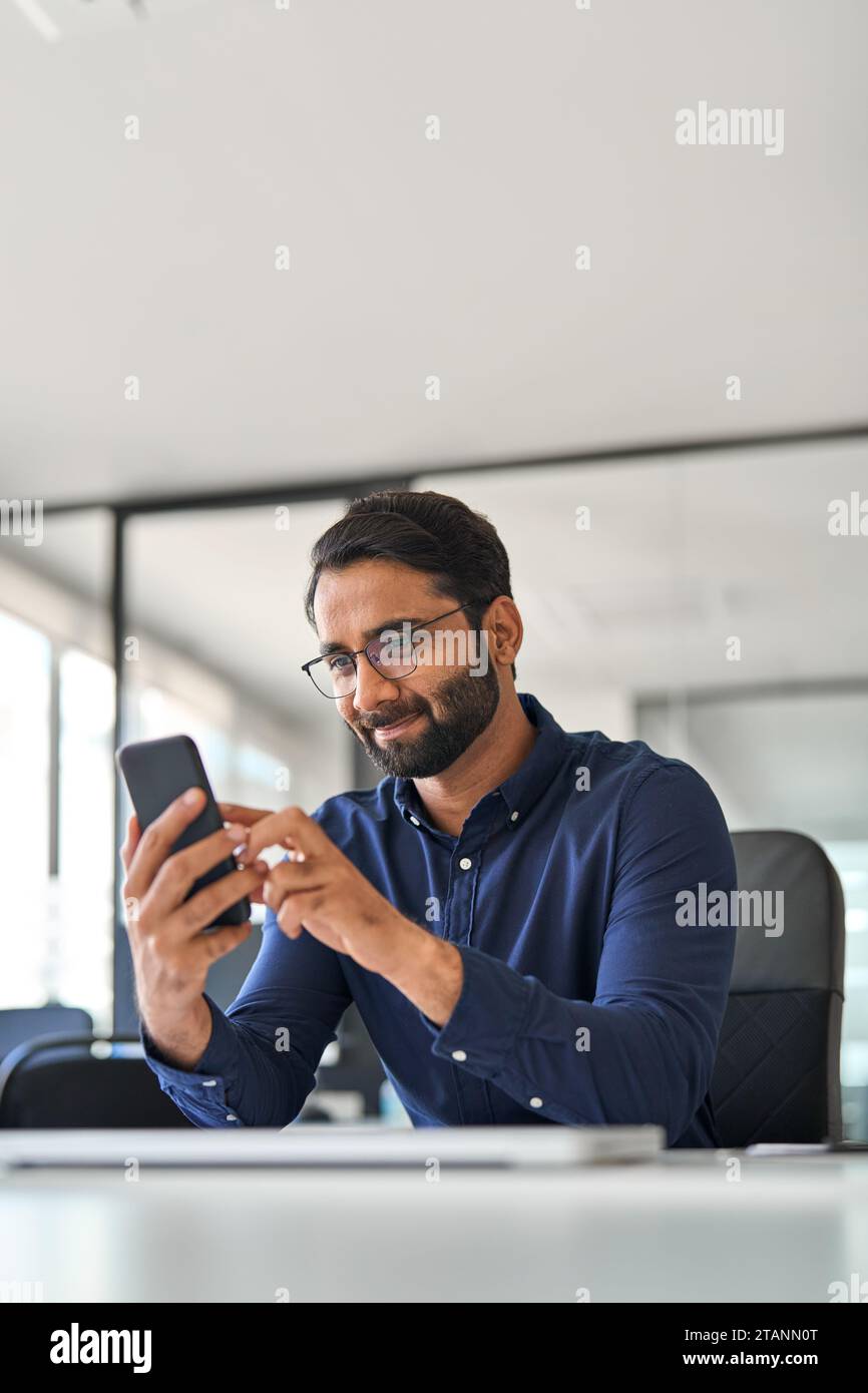 Professional Indian businessman office worker using cellphone at work. Vertical Stock Photo