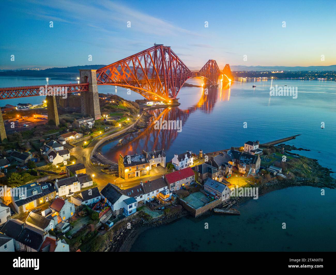 Aerial view from drone at night of North Queensferry village beside the Forth Bridge crossing the Firth of Forth, Fife, Scotland, UK Stock Photo