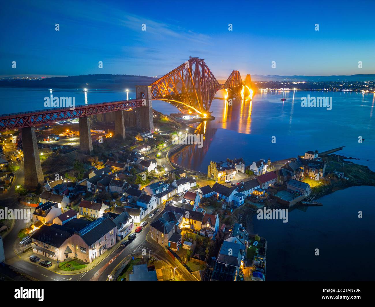 Aerial view from drone at night of North Queensferry village beside the Forth Bridge crossing the Firth of Forth, Fife, Scotland, UK Stock Photo