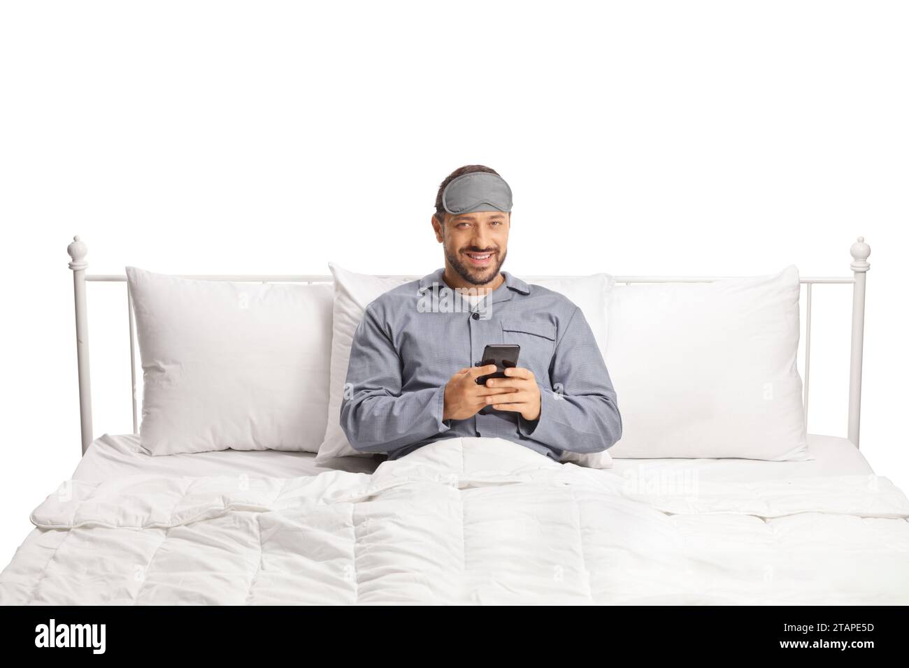 Man in pajamas sitting in a bed and holding a smartphone isolated on white background Stock Photo