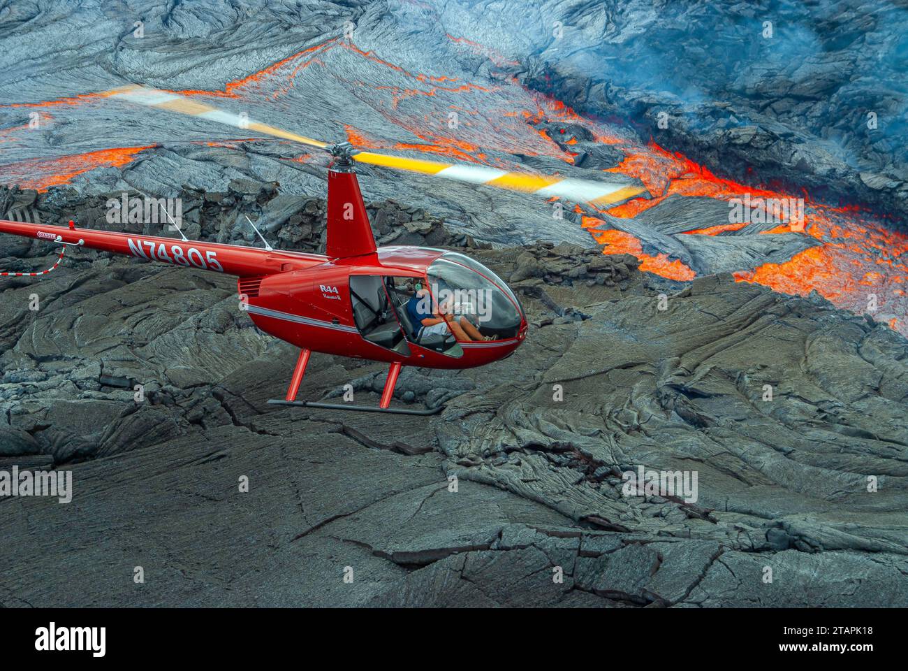 An air-to-air view of a red Robinson R44 helicopter, flying low over a ...