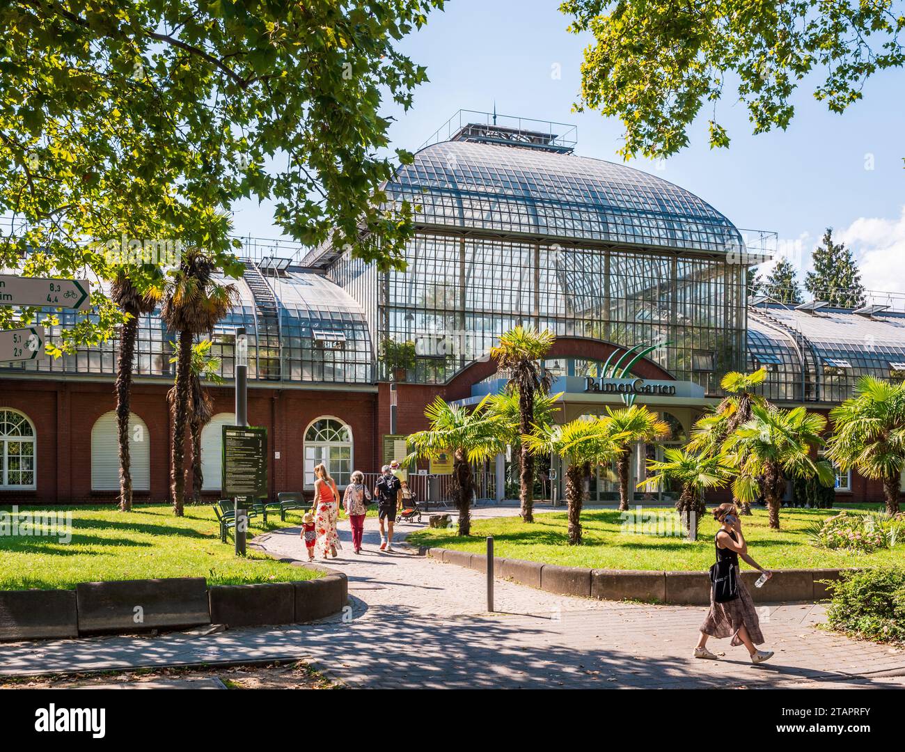 People head towards the main entrance of the Palmengarten in Frankfurt am Main, Germany, on a sunny summer afternoon. Stock Photo