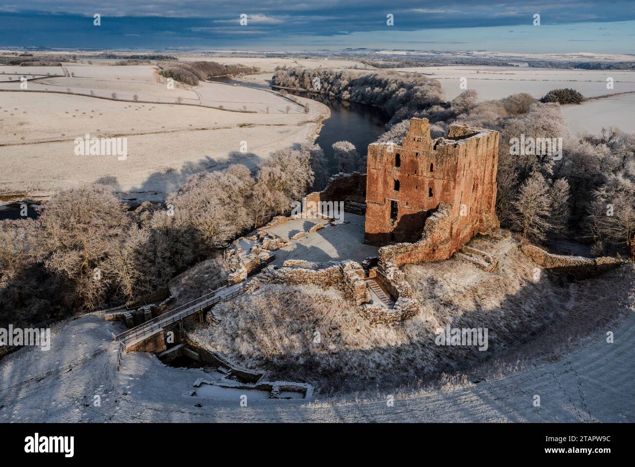 A snow covered landscape with Norham Castle in winter sunshine, sits high above the River Tweed guarding the border. Norham, Northumberland, England Stock Photo