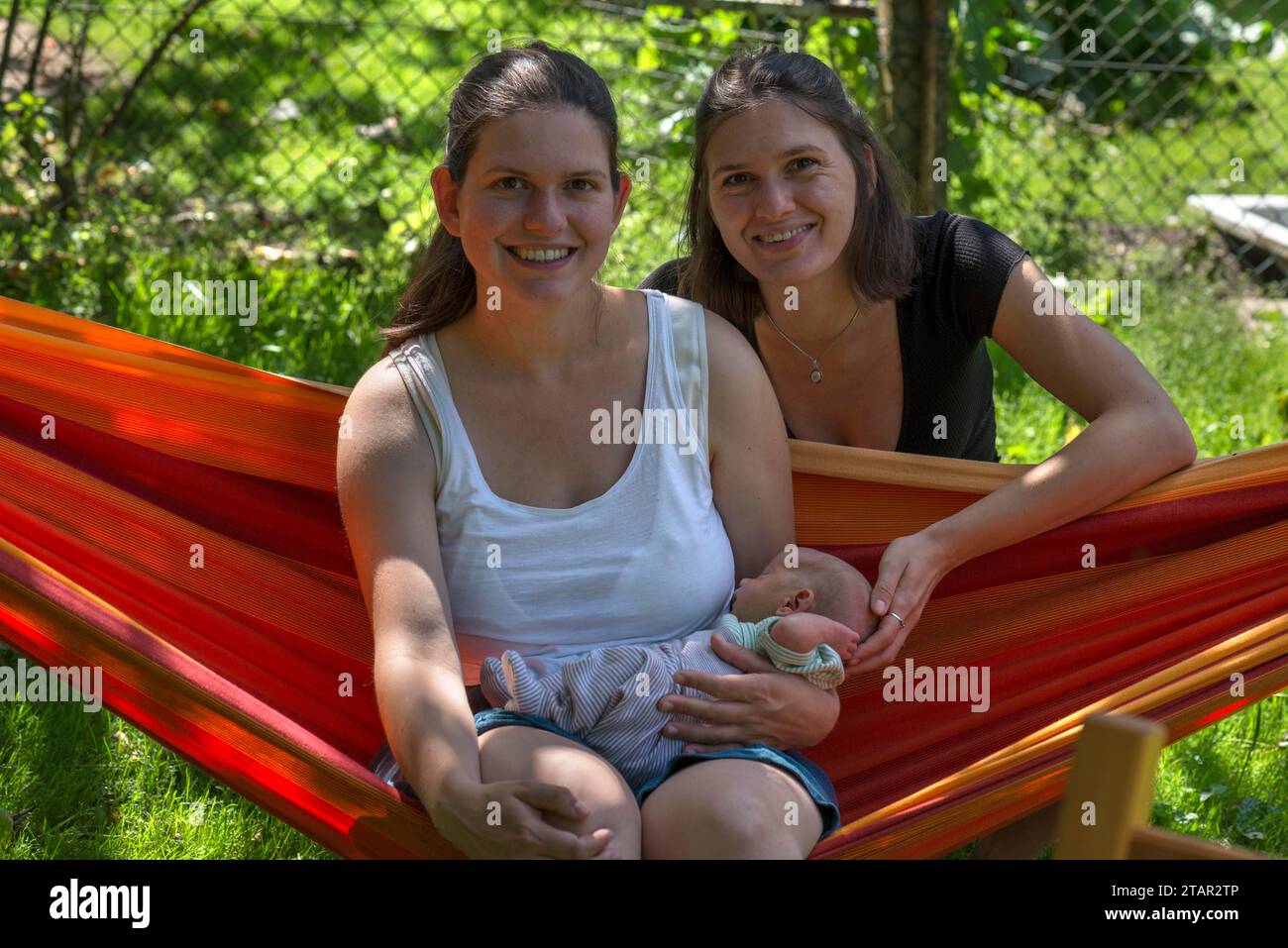 Young mother with baby in a hammock in the garden, her sister in the background, Mecklenburg-Vorpommern, Germany Stock Photo