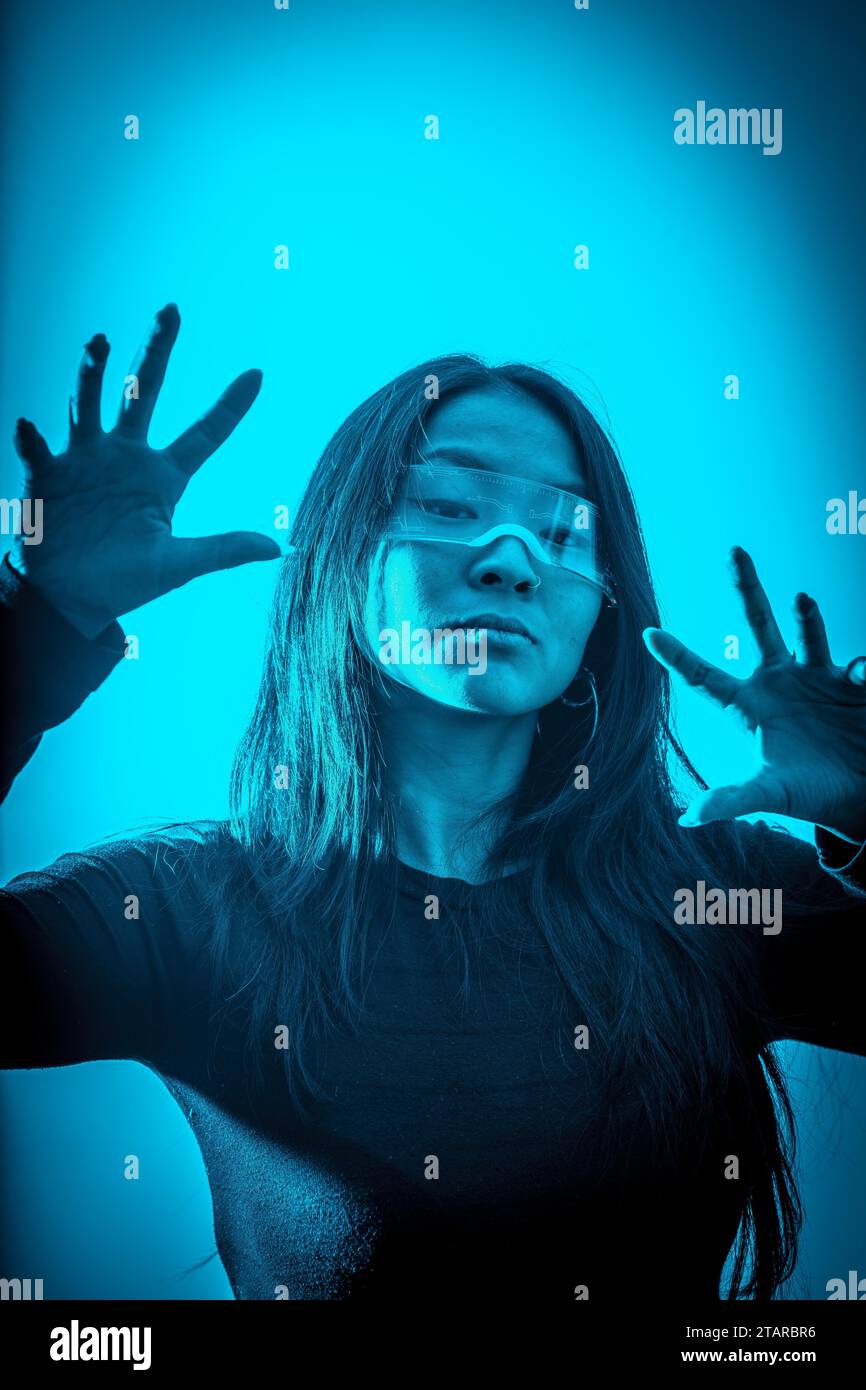 Studio photo with blue background with neon lights of a cyber chinese woman gesturing in a metaverse space Stock Photo