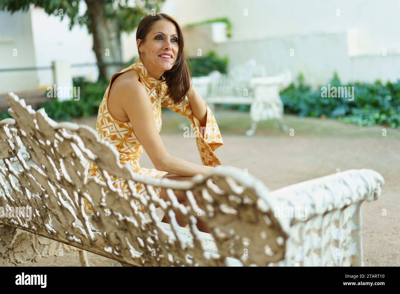 Concentrated young woman sitting on white bench in park Stock Photo