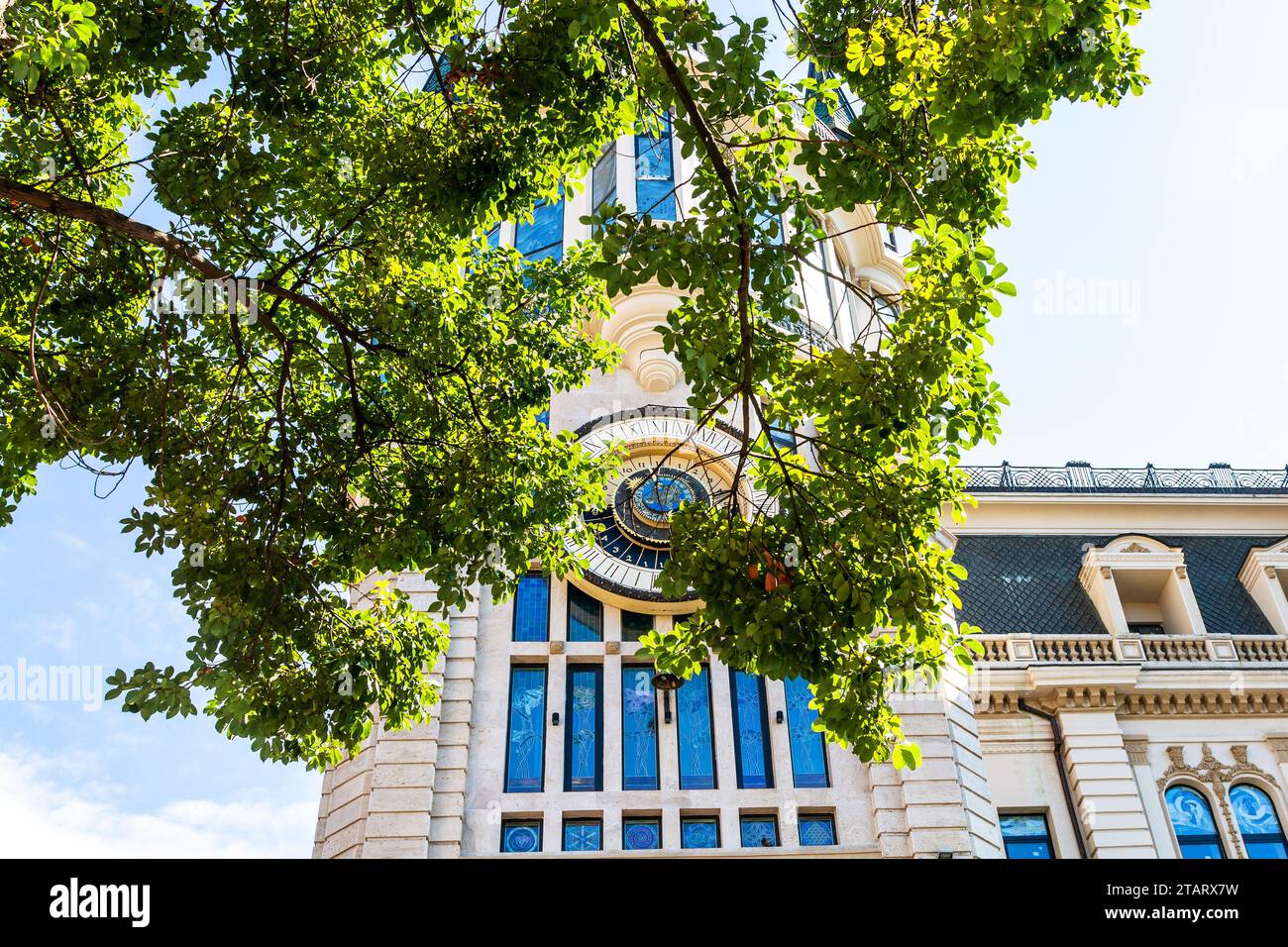 Batumi, Georgia - September 15, 2023: green branch of tree and Astronomical Clock on tower of formerly building of National Bank of Georgia on backgro Stock Photo