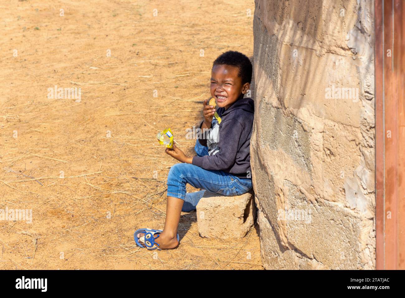hungry african child eating biscuits , african village homestead yard with shack Stock Photo