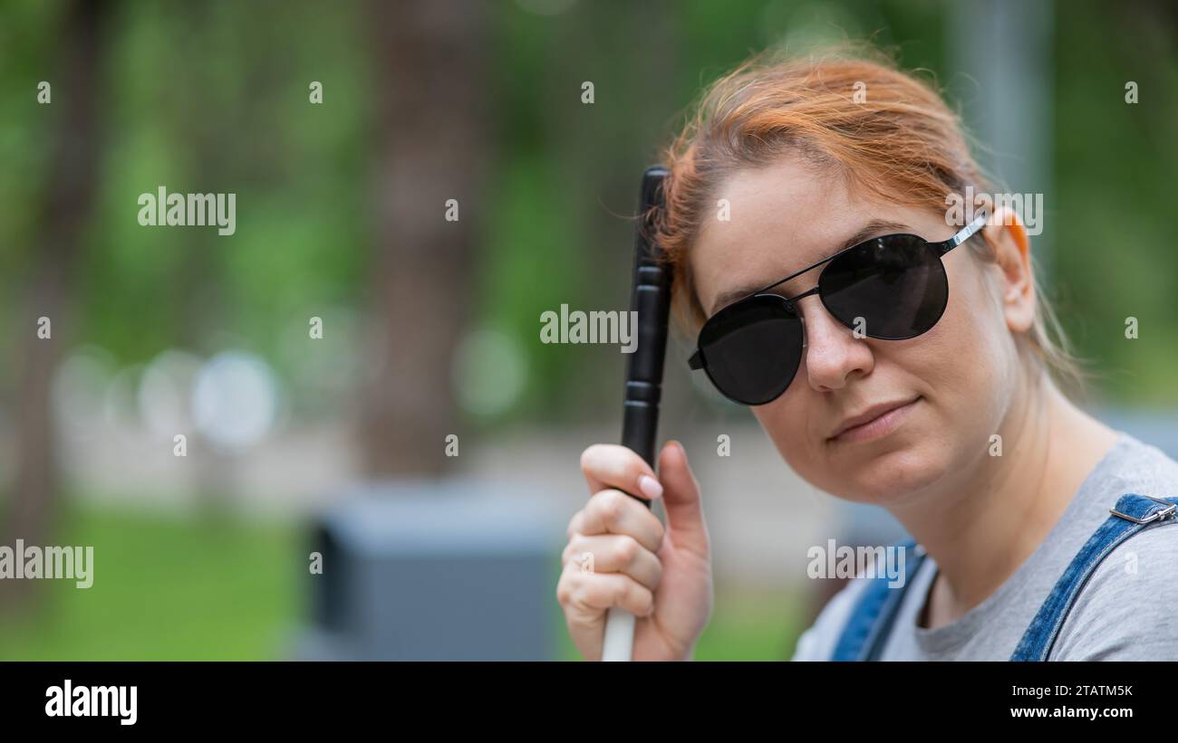 Blind red-haired woman sitting outdoors leaning on a cane. Stock Photo