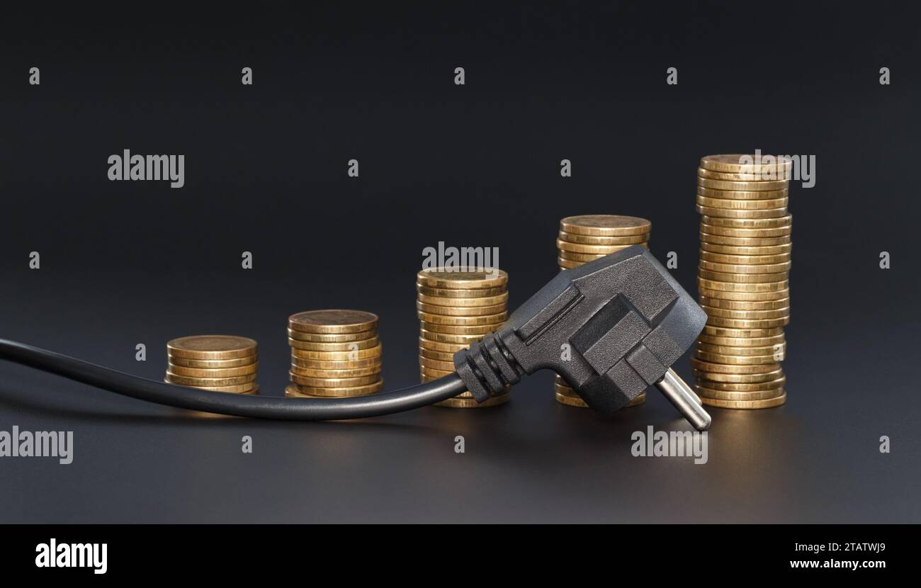 An electric plug against a background of stacks of coins, in the form of a growing diagram on a dark background. The concept of increasing electricity Stock Photo