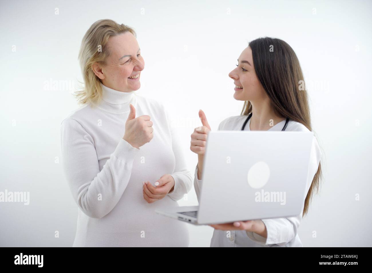 young girl doctor showing thumb up to woman patient woman happy also showing class she is all healthy and happy helped medicines white background  Stock Photo