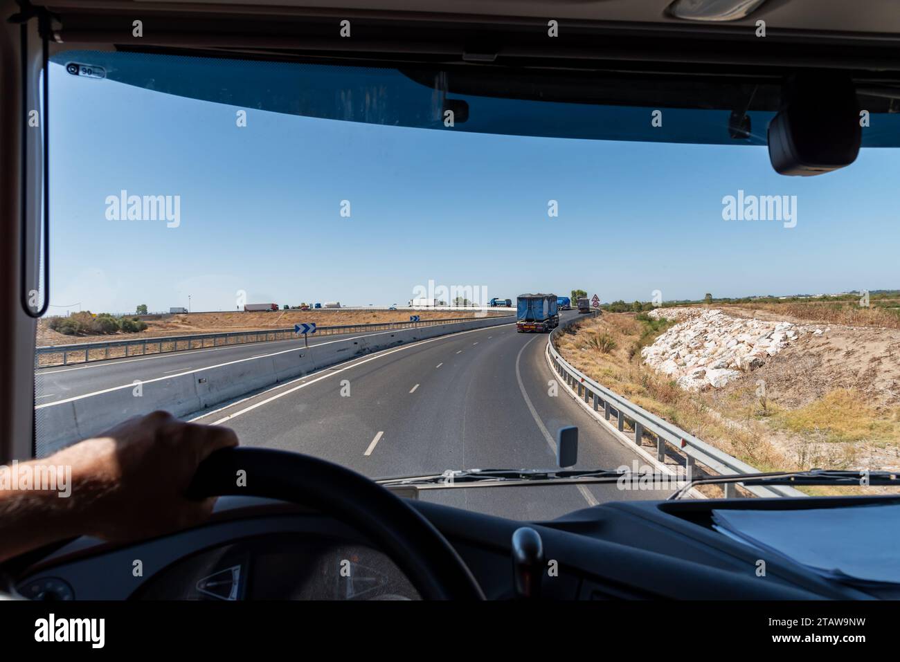 View from inside a truck of a curved road with a lot of heavy traffic in both directions. Stock Photo