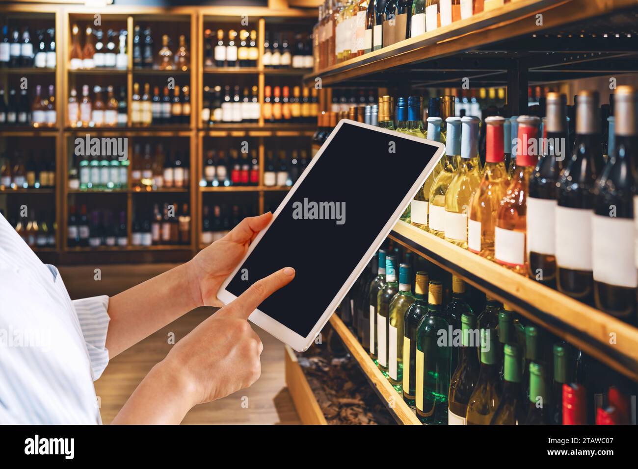 Liquor store manager using digital tablet in front of half of wine bottles. Blank screen of computer tablet and wine shop. Stock Photo