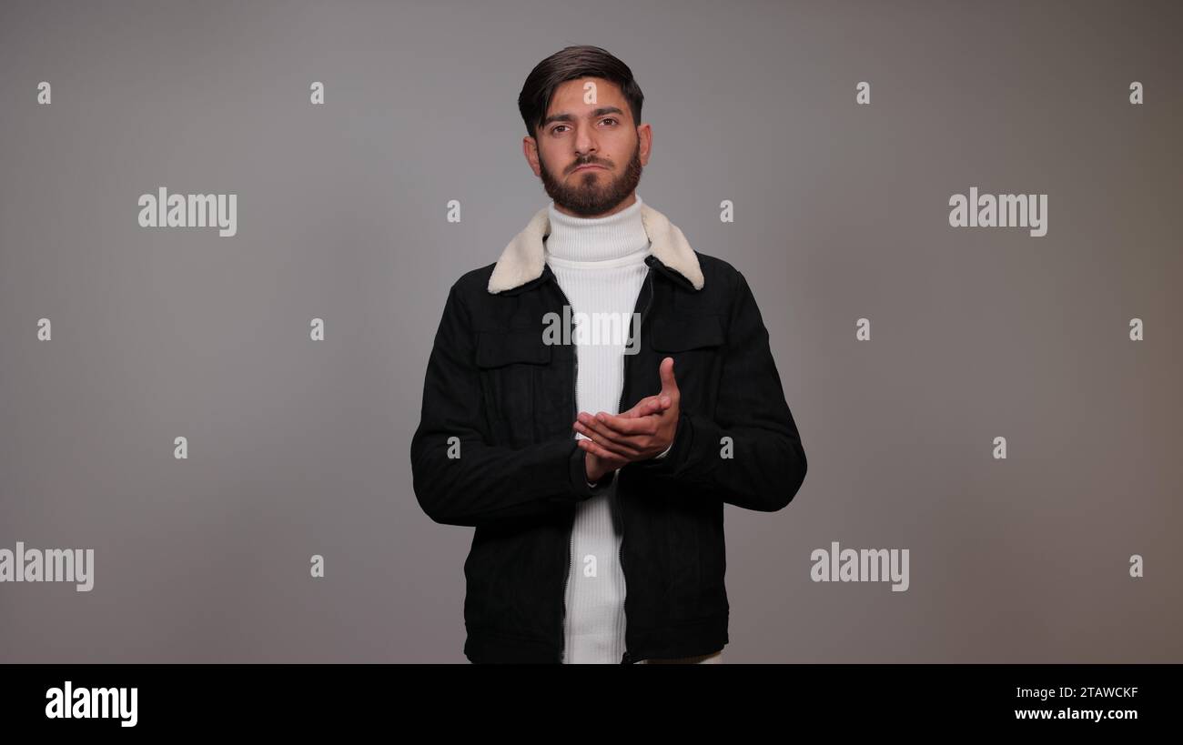 A young man clapping his hands against a gray background. Stock Photo