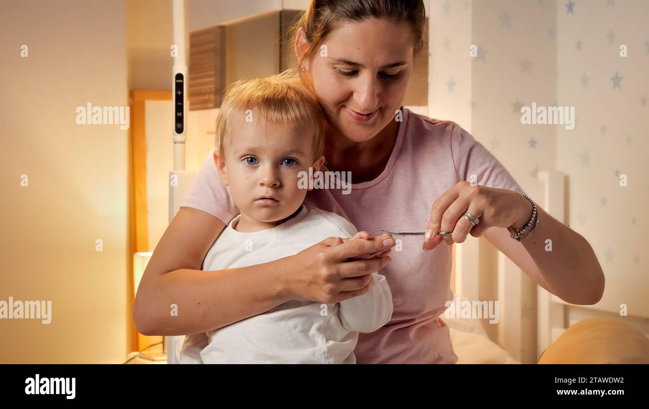 Little baby boy sitting on mothers lap while she is cutting his fingernails. Parenting, child hygiene and healthcare, going to sleep Stock Photo