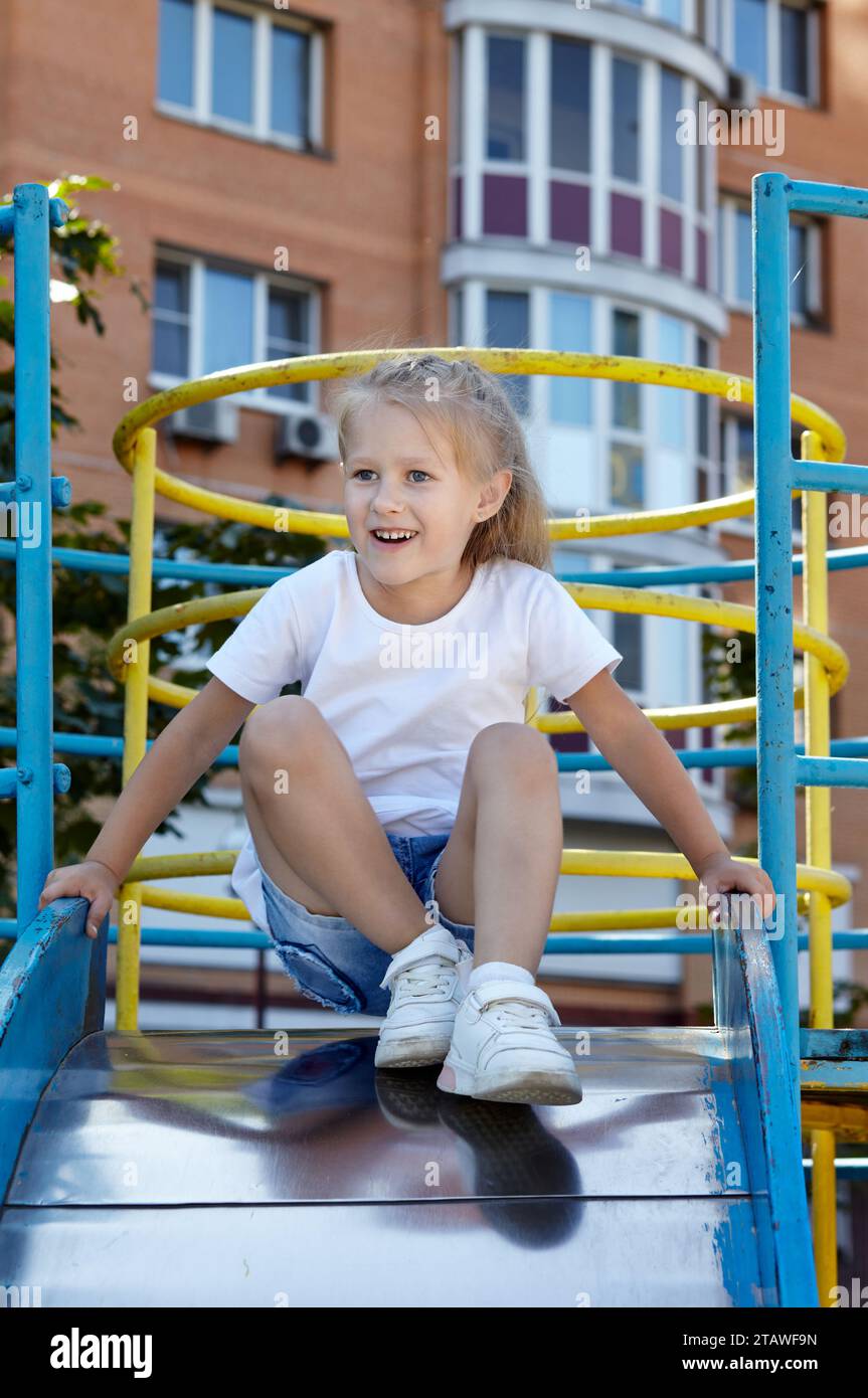 Little girl playing on a slide in a playground in the summer city park ...