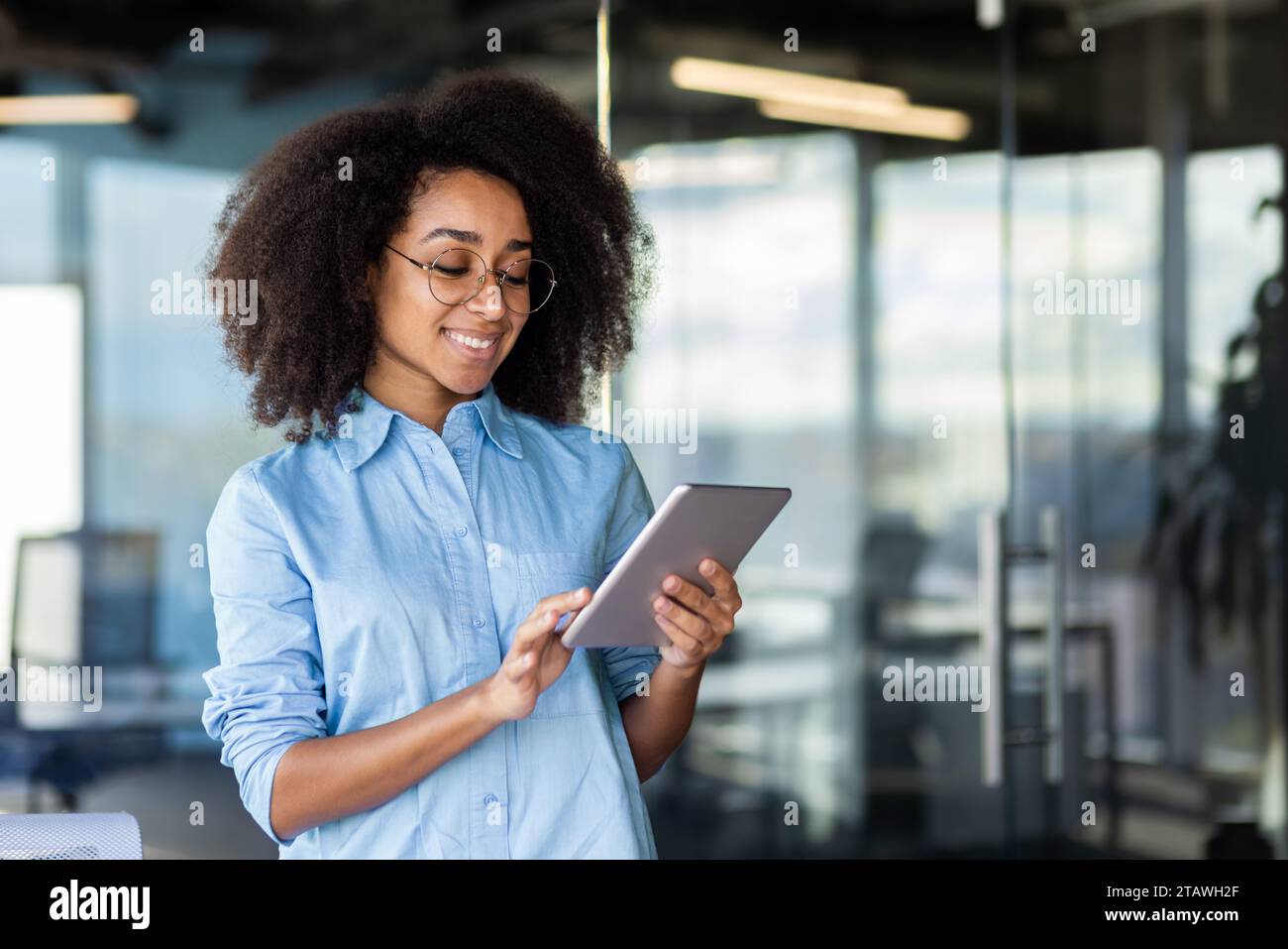 Young beautiful successful woman at workplace inside office with tablet computer in hands, female programmer testing new app, happy smiling. Stock Photo