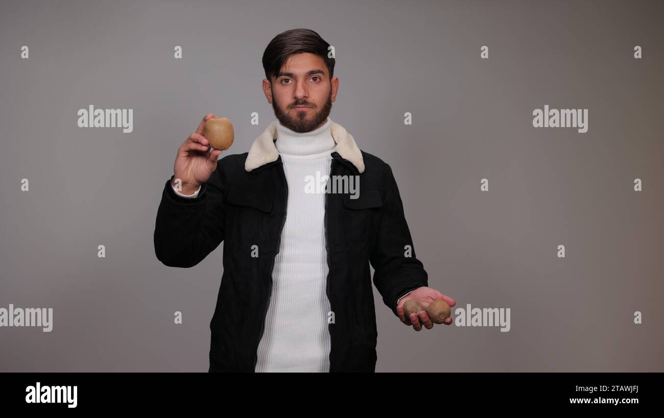A young man against a gray background promoting and encouraging people to eat kiwi | advantage of kiwi Stock Photo