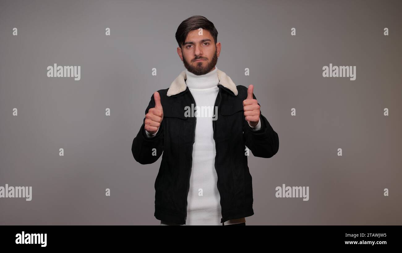 Young man isolated on a gray background, posing with a thumbs-up towards the camera, showing a 'like.' Stock Photo