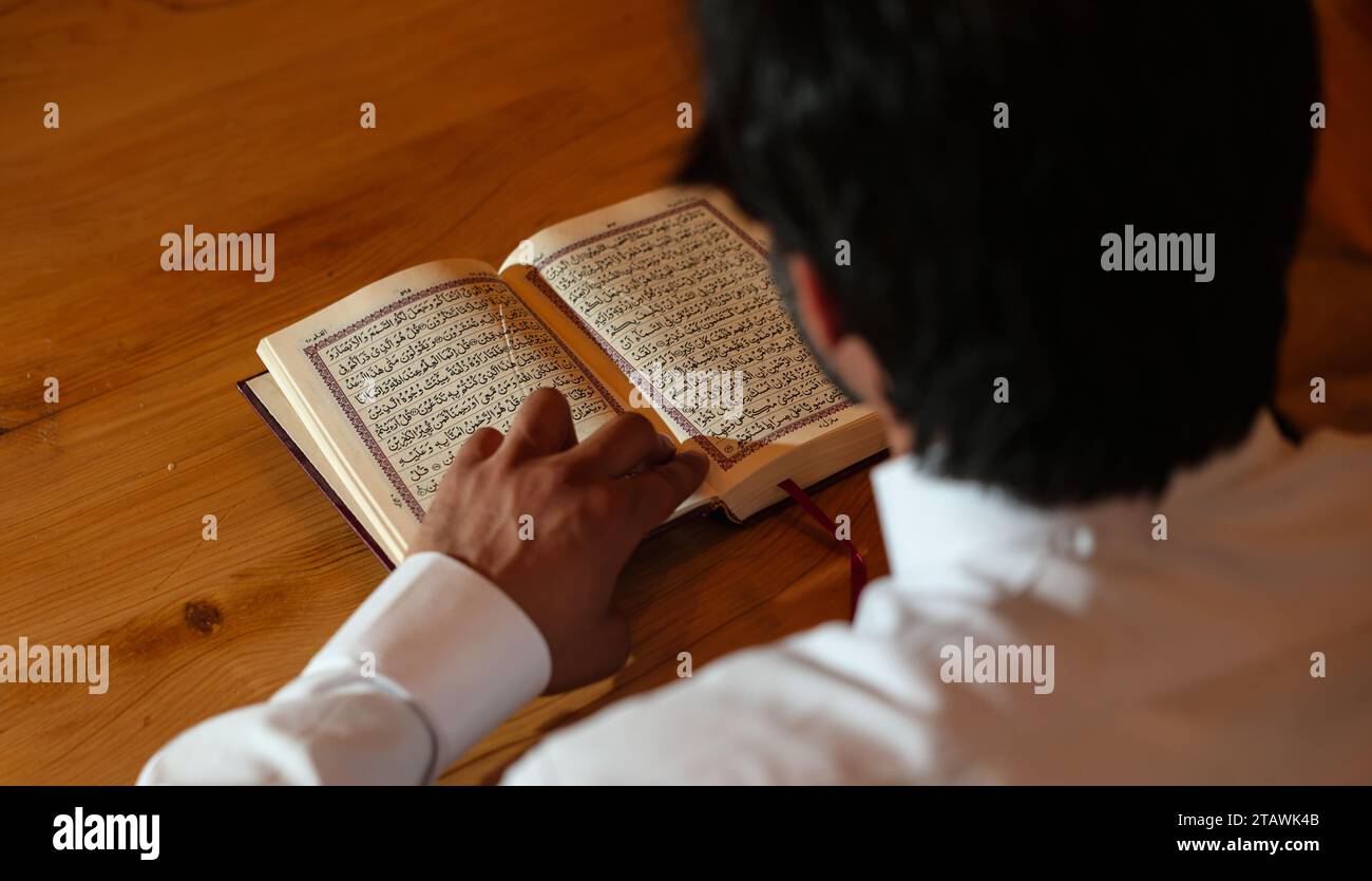 Muslim man reading holy Quran. Holy Quran in Hand with Arabic text meaning of Al Quran. Stock Photo