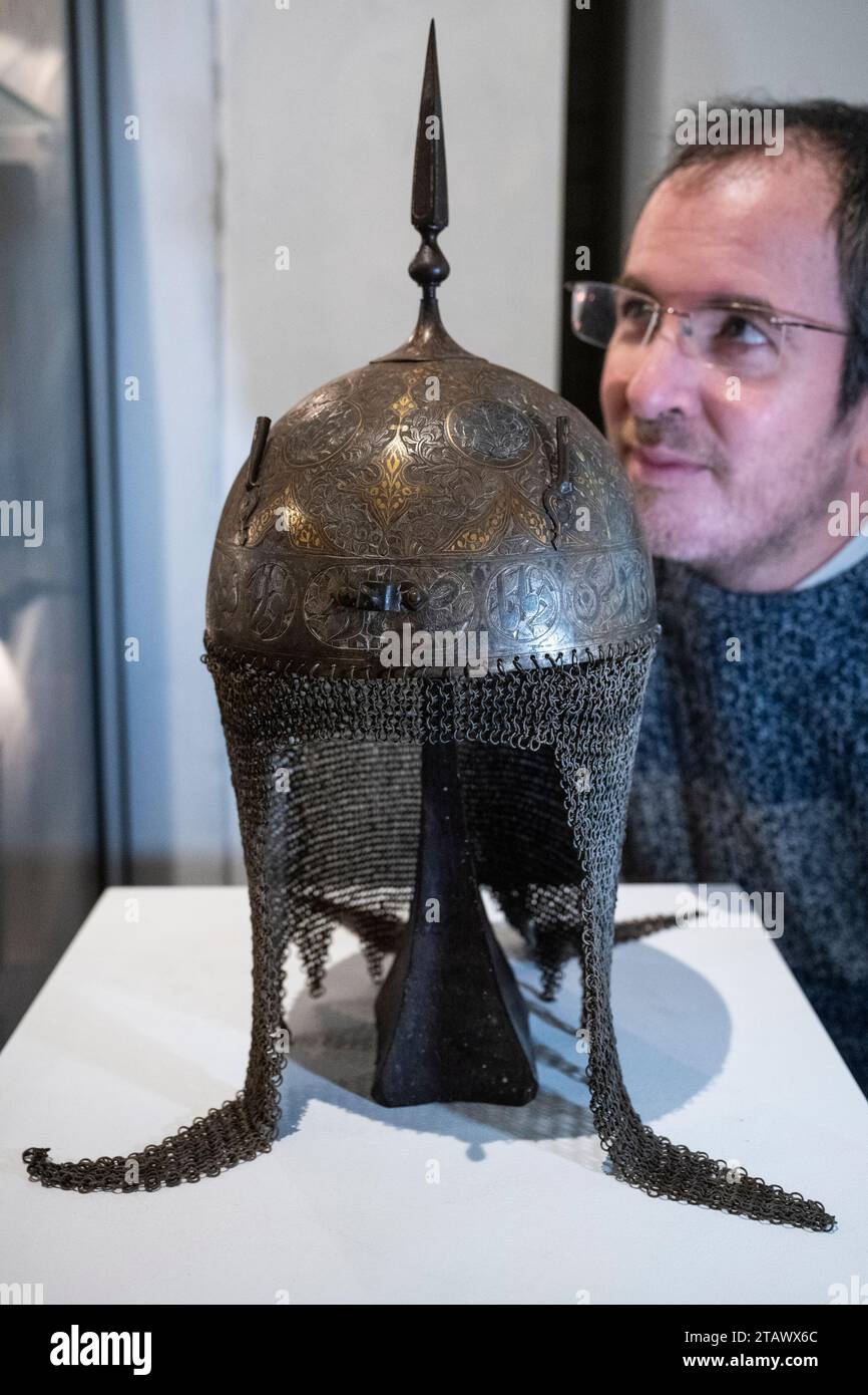London, UK.  3 December 2023. A staff member inspects ‘A Persian decorated helmet (kulah khud)’, Qajar, mid-19th century (Est. £800 - £900) at a preview of highlights from the upcoming Arms, Armour and Militaria sale at Olympia Auctions in west London.  The sale takes place on 6 December.  Credit: Stephen Chung / Alamy Live News Stock Photo