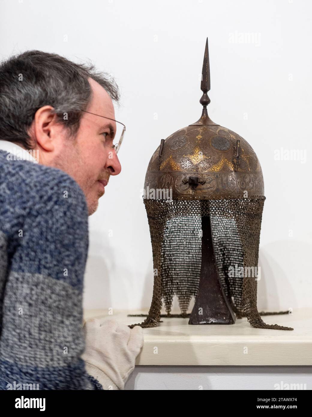 London, UK.  3 December 2023. A staff member inspects ‘A Persian decorated helmet (kulah khud)’, Qajar, mid-19th century (Est. £800 - £900) at a preview of highlights from the upcoming Arms, Armour and Militaria sale at Olympia Auctions in west London.  The sale takes place on 6 December.  Credit: Stephen Chung / Alamy Live News Stock Photo
