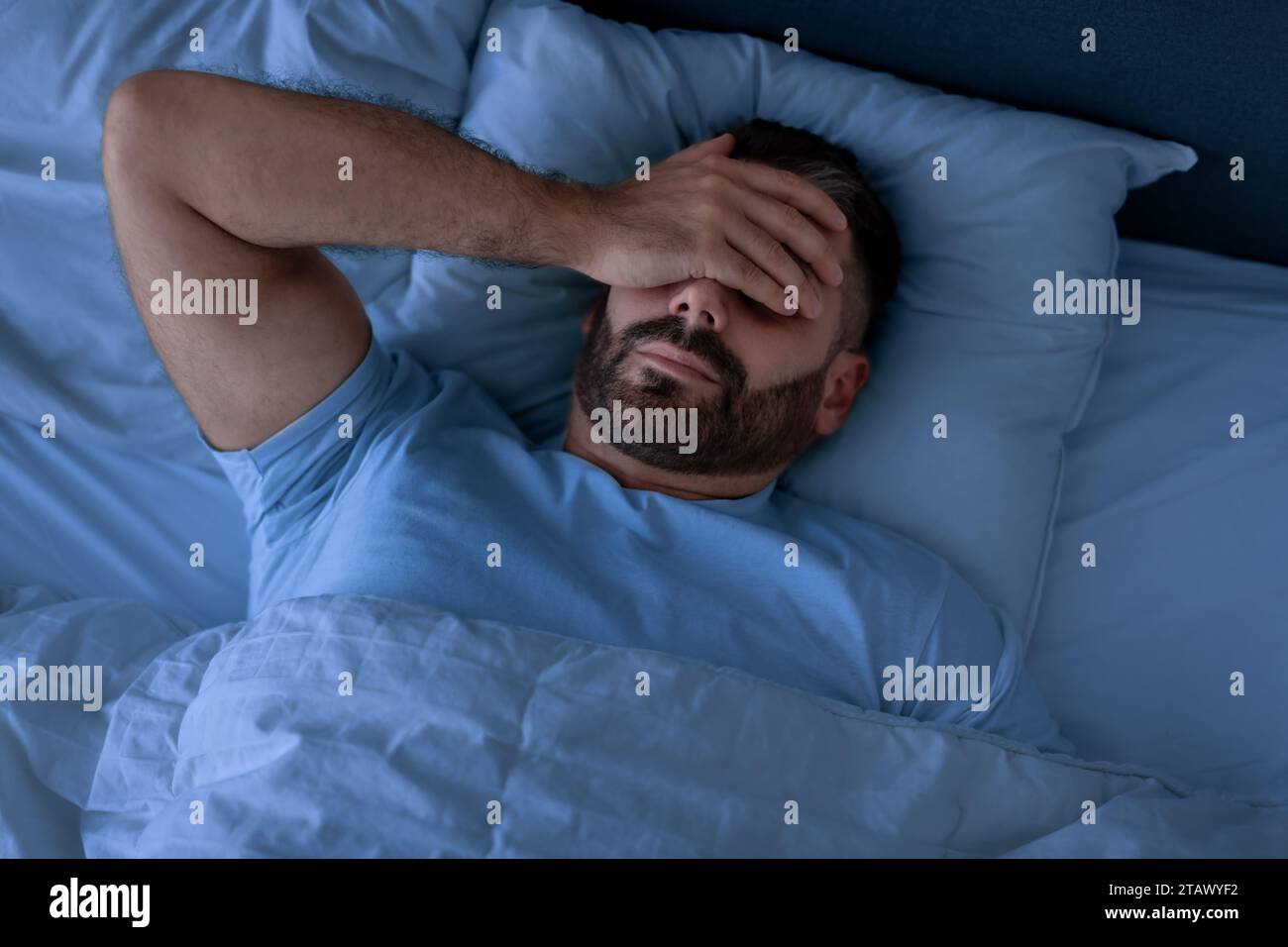 Man Covering Face With Hand Lying Not Sleeping In Bedroom Stock Photo