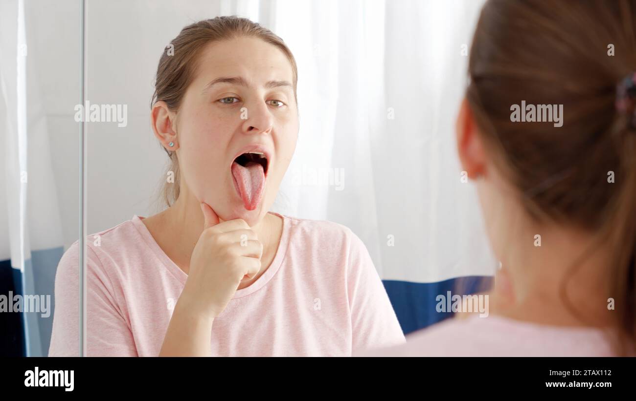 Portrait Of Young Woman Checking Her Teeth And Tongue For Plaque At Mirror In Bathroom Concept 