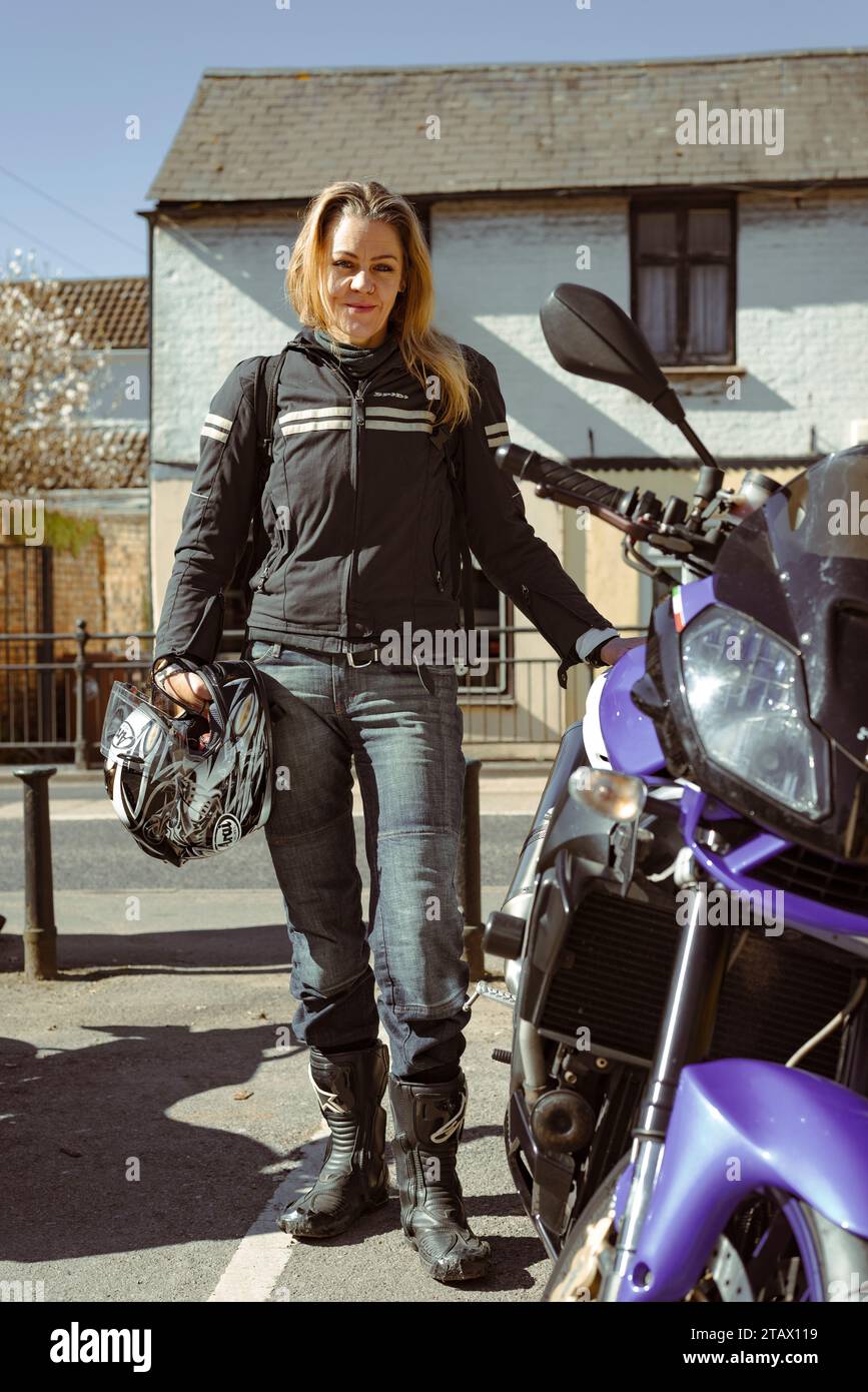 A woman in biker gear stands proudly with her 1000cc motorbike in the English countryside in Hertfordshire in the UK Stock Photo